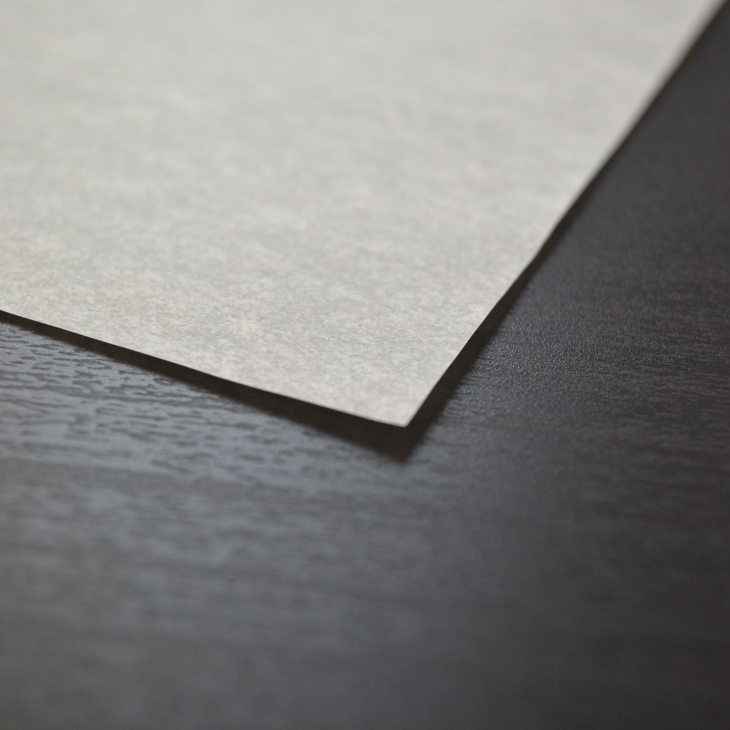 Close-up of a textured beige paper sheet on a dark surface